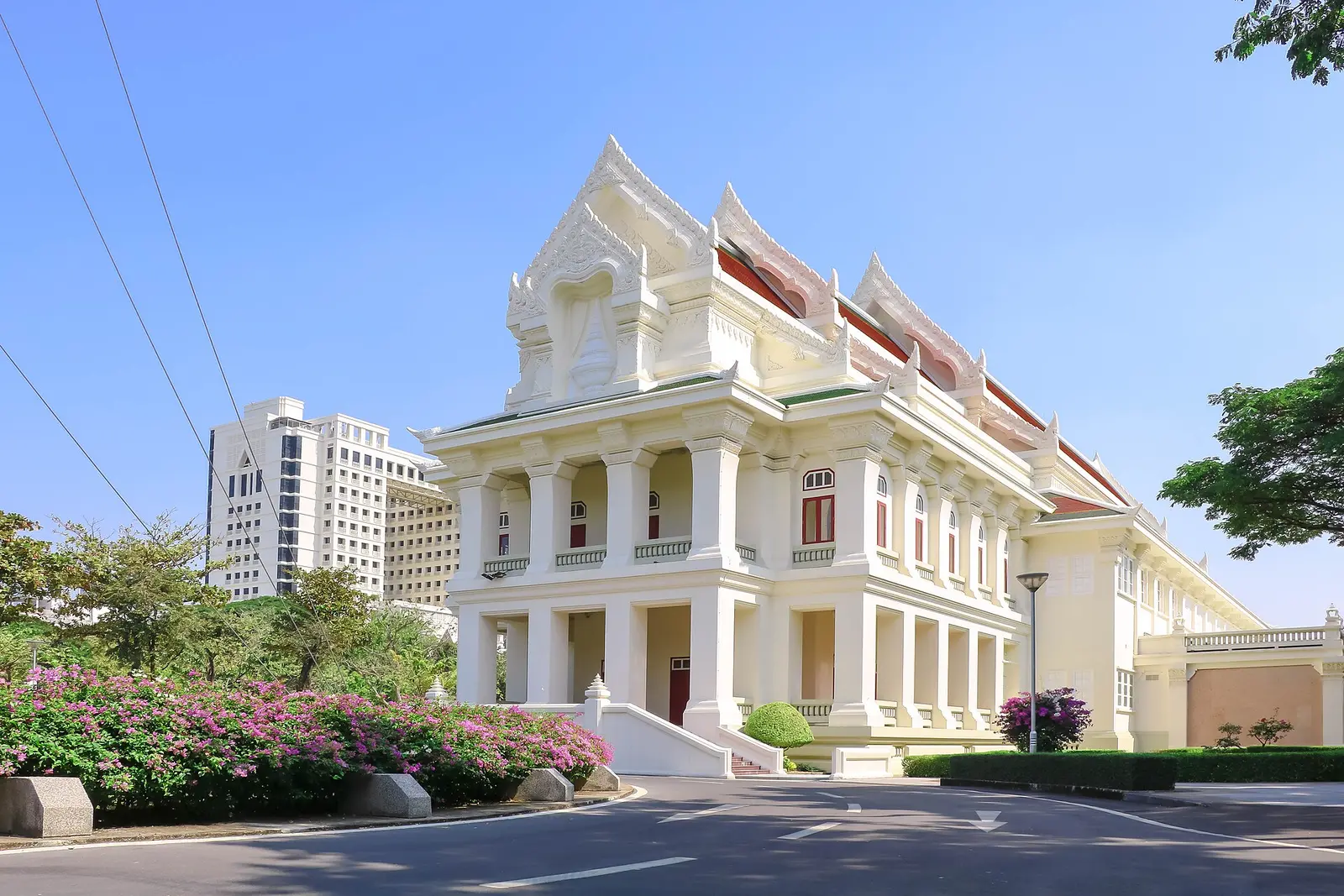 Chulalongkorn University Auditorium, a white Thai style building with flowering shrubs