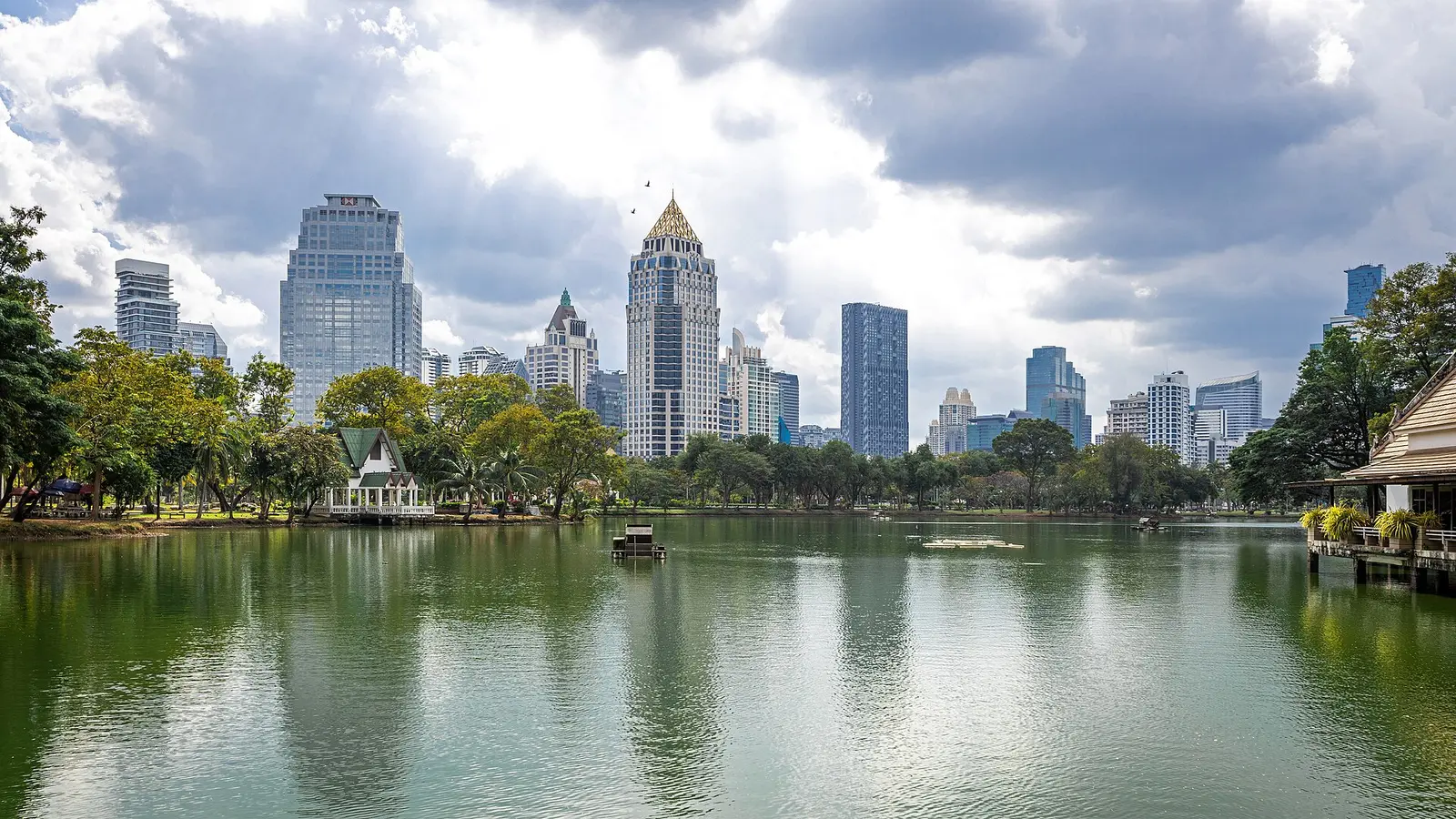 Lake in Lumphini Park with Bangkok towers reflected behind the trees