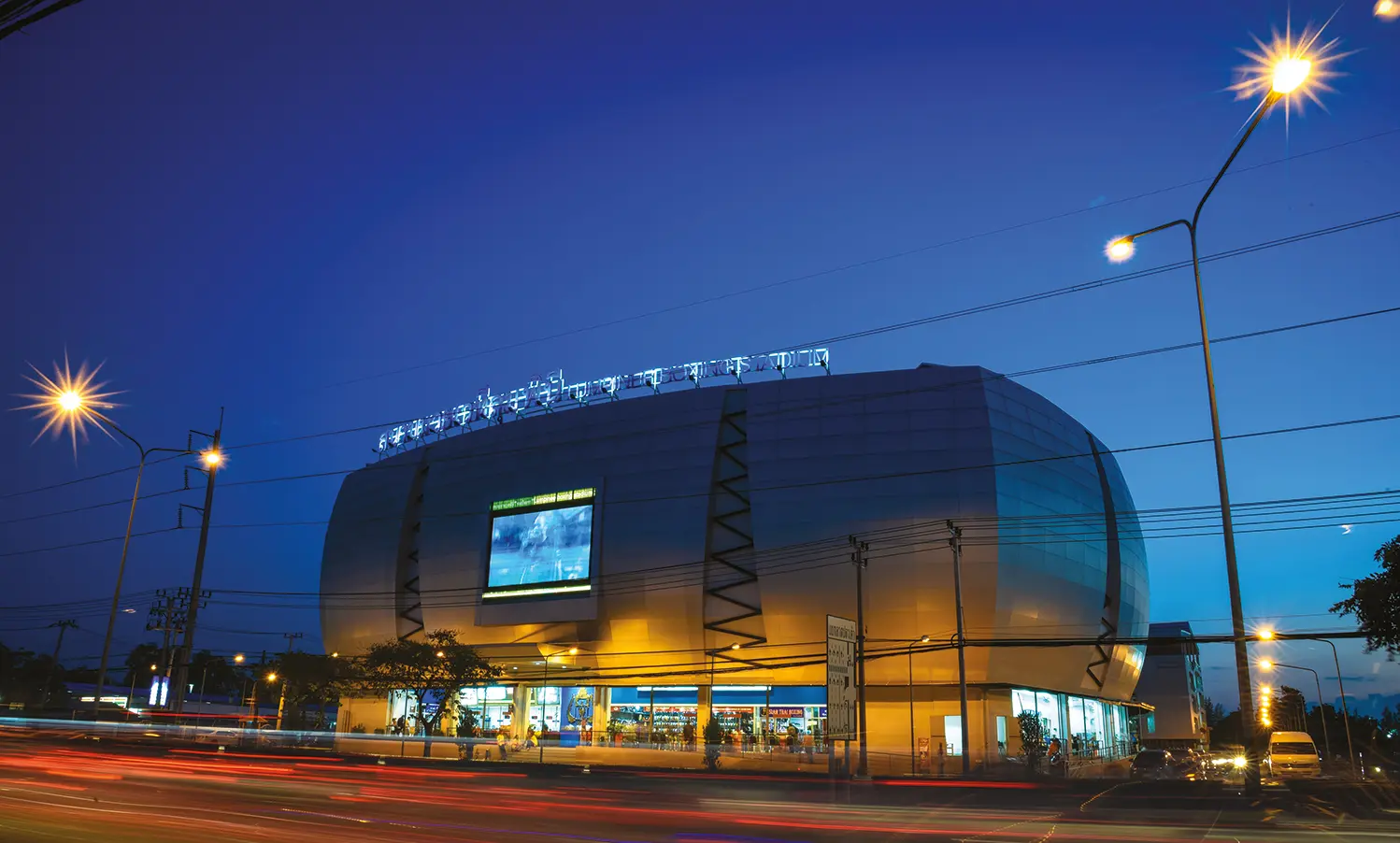 Lumpinee Boxing Stadium exterior lit at dusk with light trails on the road