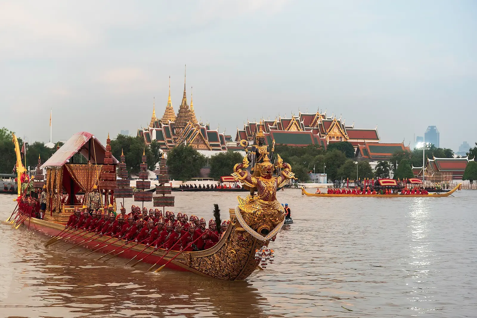 A gilded royal barge on the Chao Phraya River with the Grand Palace behind during a 2024 rehearsal