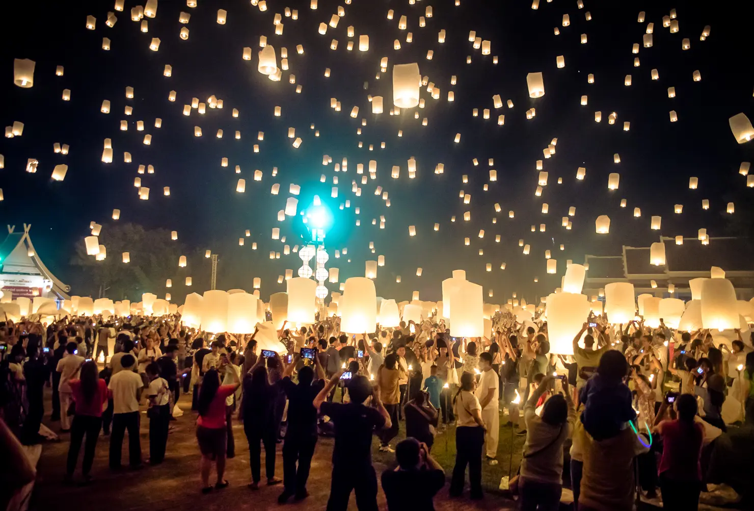 Crowd releasing glowing paper lanterns into the night sky at the Yi Peng festival in Chiang Mai